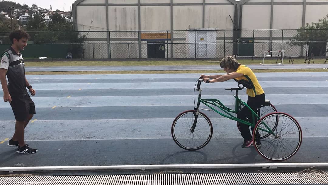 Foto minha e da Kamila na pista da UFSC. A foto é lateral, estou a frente da Kamila que está na petra, orientado ela na atividade.