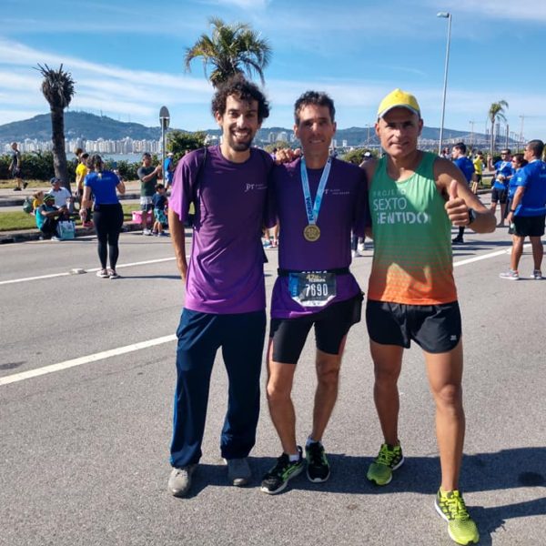 Eu, Gilmar e Leandro apos a Maratona. Em pé no asfalto, ao fundo beira mar continental, os dois com suas medalhas.