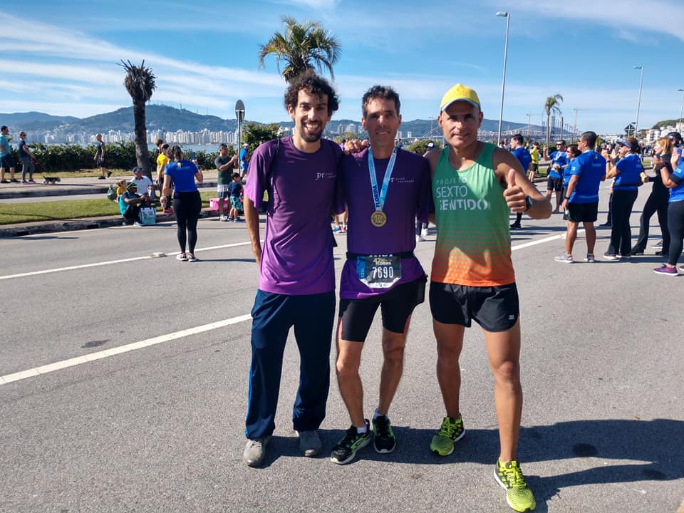 Eu, Gilmar e Leandro apos a Maratona. Em pé no asfalto, ao fundo beira mar continental, os dois com suas medalhas.